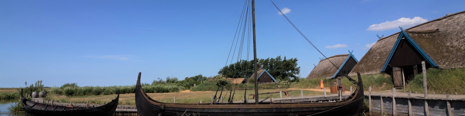 A traditional boat docked by a riverbank with thatched-roof buildings in the background.