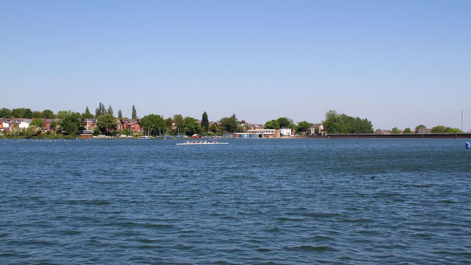 Ein ruhiger Fluss mit einem Ruderboot in der Ferne, umgeben von Häusern und Bäumen.
