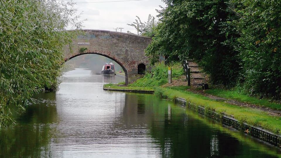 Wiggins Hill Bridge near Curdworth, Warwickshire Birmingham and Fazeley Canal. The original purpose of this canal was to provide a link between Birmingham and the south east of England, by way of the Coventry Canal and the Oxford Canal. John Smeaton was the engineer, and the canal was completed in 1789. The moored narrowboat beyond the bridge is having engine problems, and has just blown out an almighty cloud of murky smoke! The bridge carries Wiggins Hill Road from the A4097 (to the right) to Over Green and Grove End.