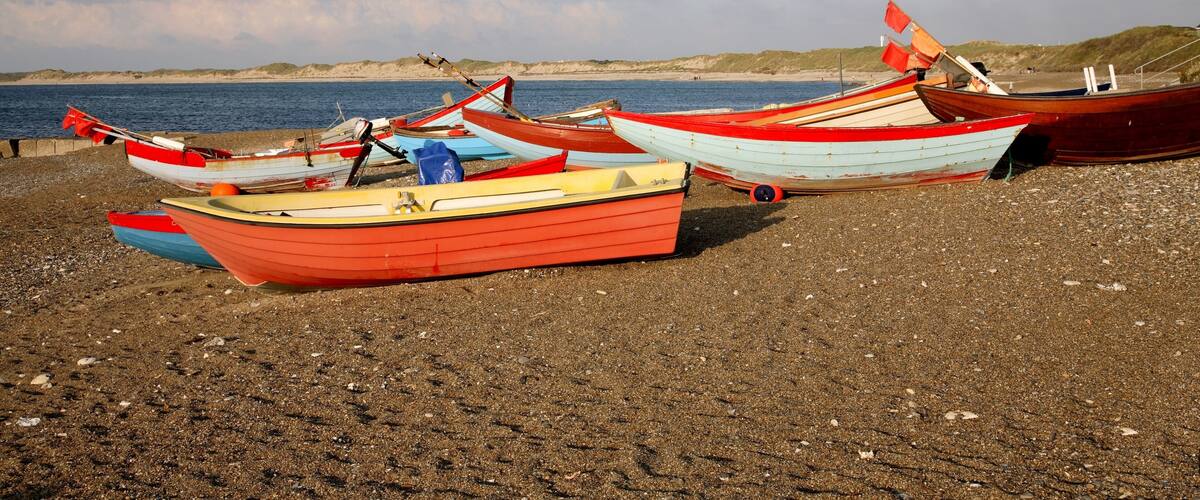 A beach with several colorful boats lined up on the shore.