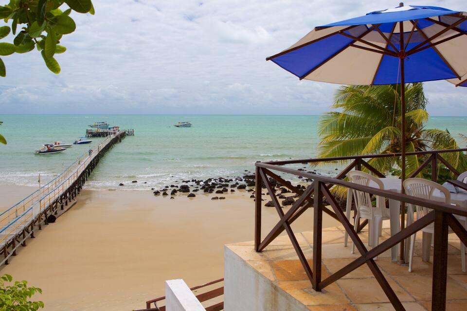 A beach with a pier, palm trees, and a blue umbrella.