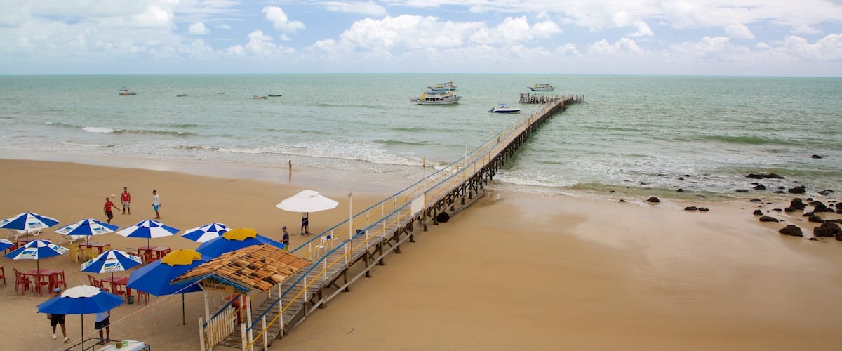 A beach with a pier extending into the water, featuring umbrellas and beach chairs.
