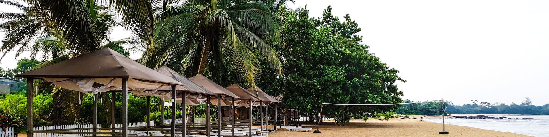 A sandy beach with white lounge chairs and shaded gazebos.