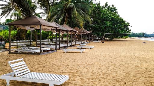 Ein sandiger Strand mit weißen Liegestühlen und beschatteten Pavillons.