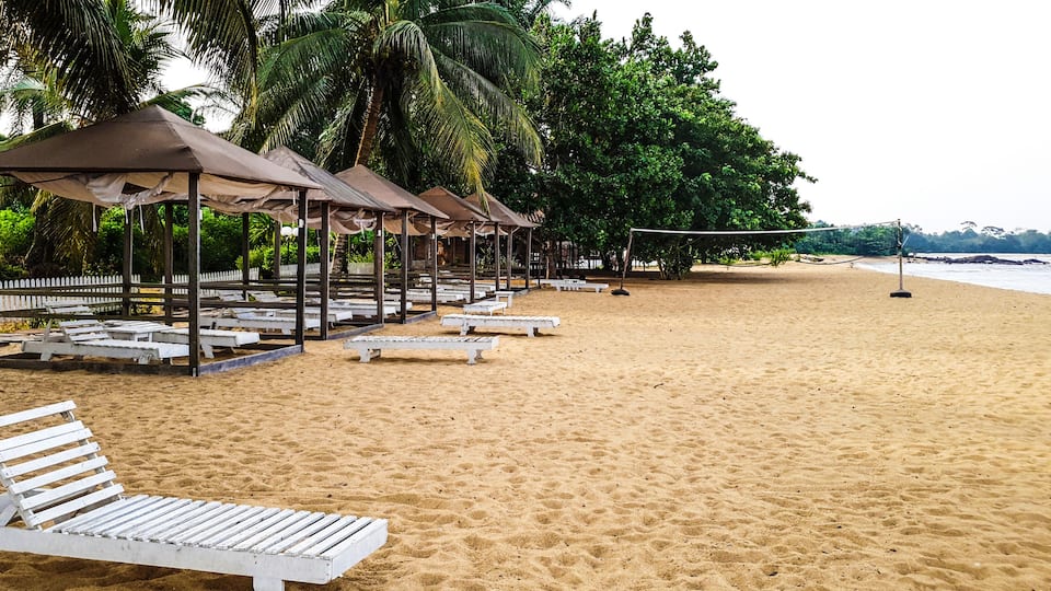 A sandy beach with white lounge chairs and shaded gazebos.
