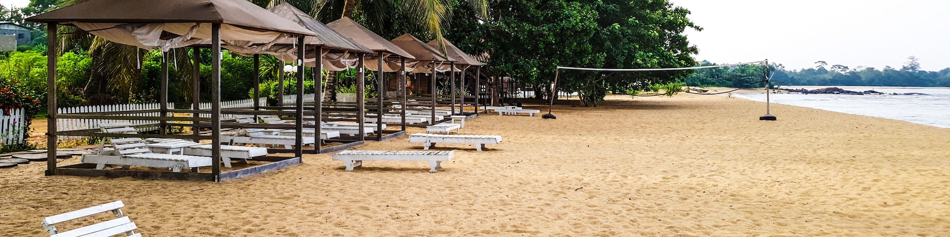 Una playa arenosa con sillas de descanso blancas y quioscos sombreados.
