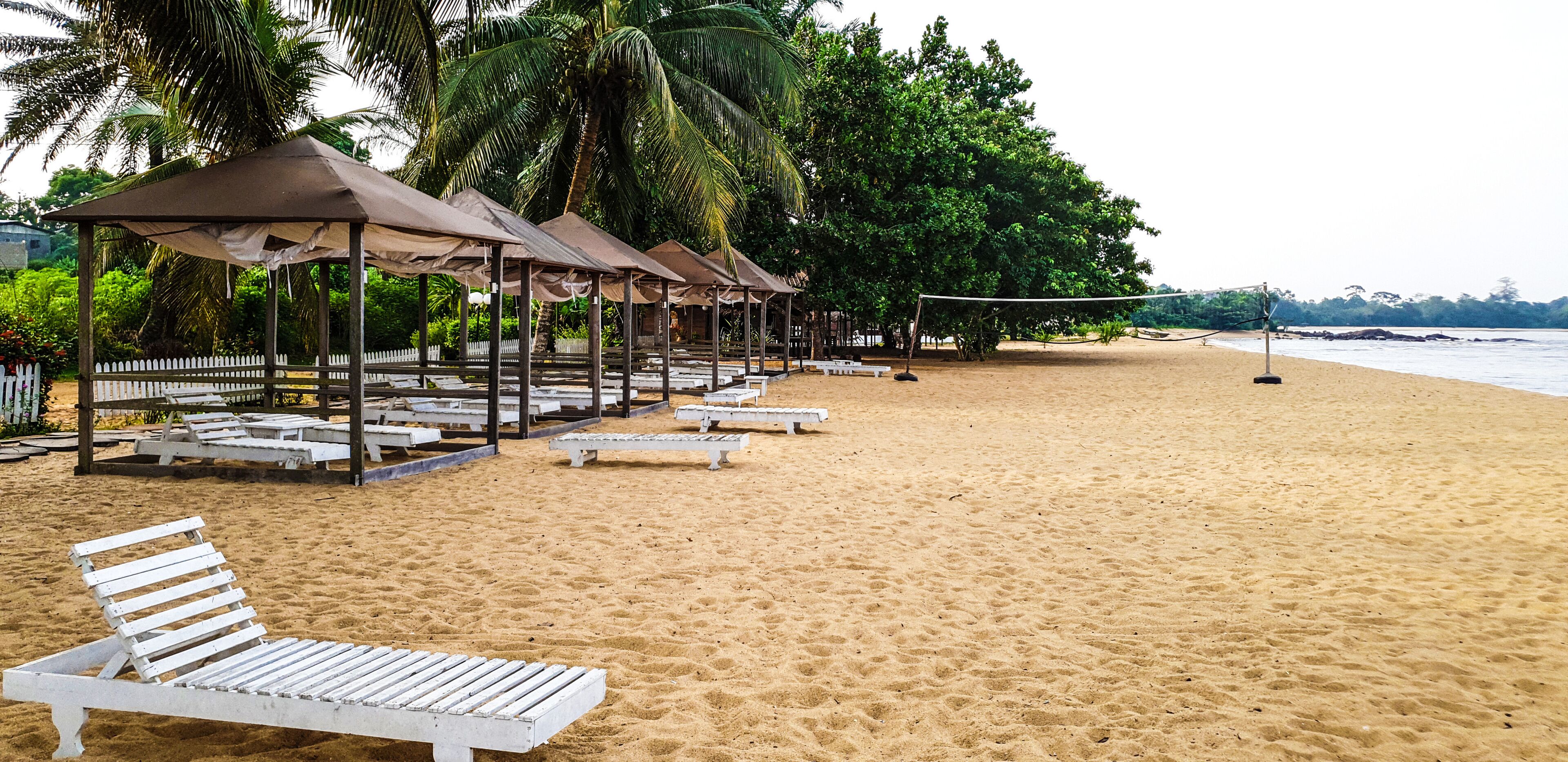 A sandy beach with white lounge chairs and shaded gazebos.