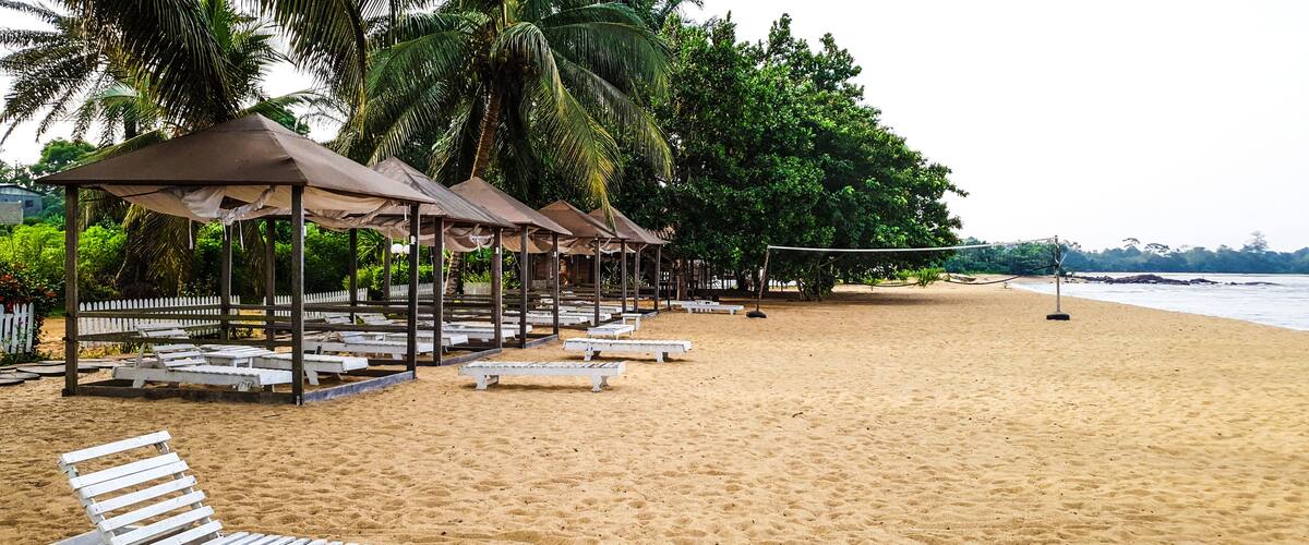 A sandy beach with white lounge chairs and shaded gazebos.