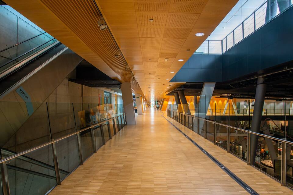 Passadís interior modern amb sòl de fusta, barana de vidre i un nivell intermèdia.