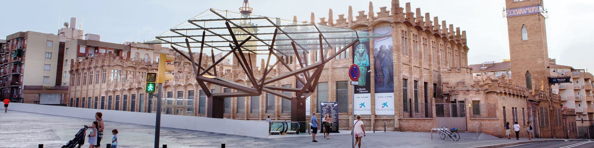A historic building with a tower, a large metal sculpture, and a pedestrian crossing.