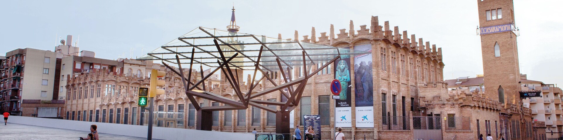 Un edificio histórico con una torre, una gran escultura de metal y un paso de peatones.
