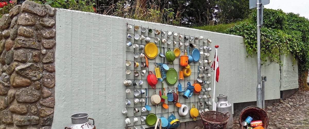 A wall with a grid of hanging dishes and a stone wall beside it.