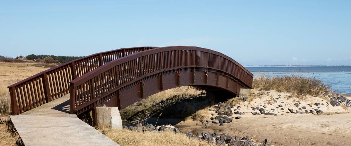 A wooden bridge over a sandy beach with a body of water in the background.