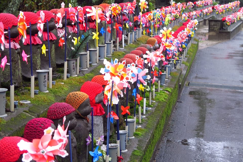 A row of colorful pinwheels and knitted hats on stone statues.