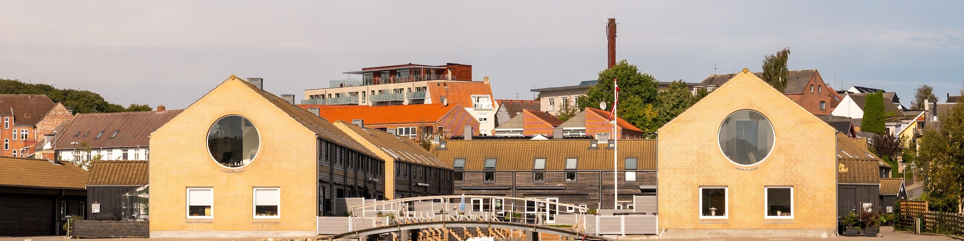 A waterfront with two yellow buildings with circular windows, a bridge, and a boat in the water.