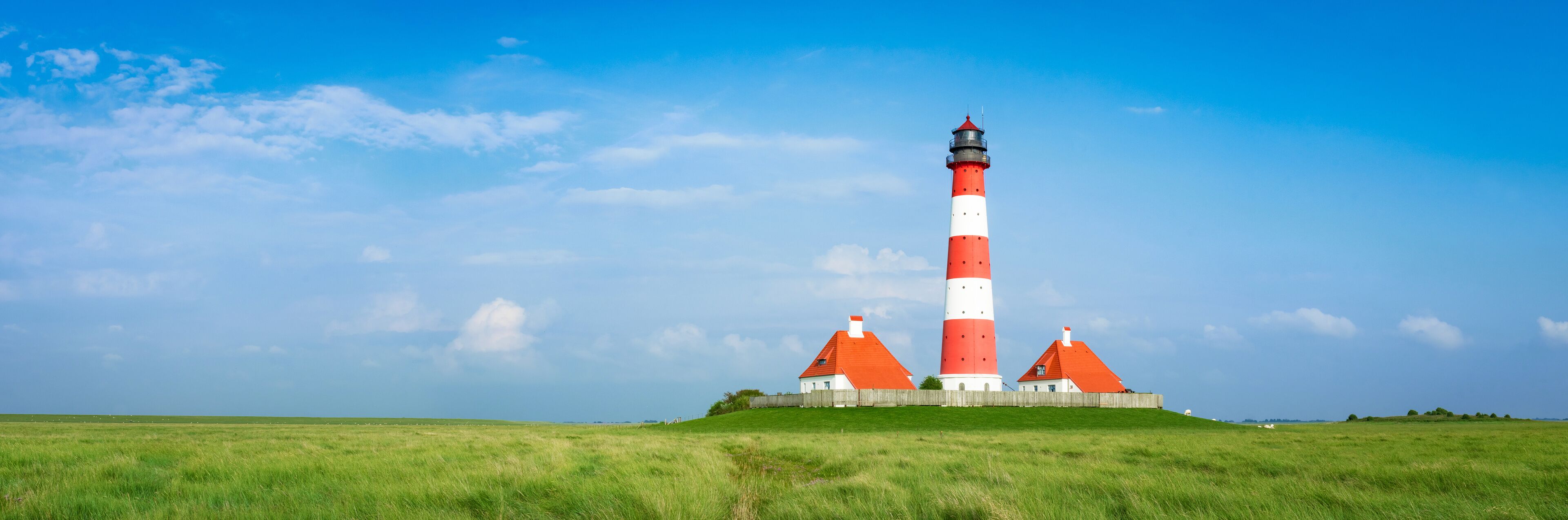 A red and white lighthouse with a wooden fence and a grassy field.