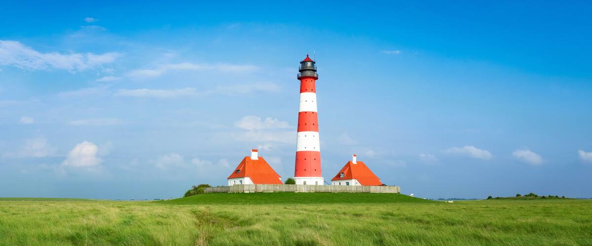 A red and white lighthouse with a wooden fence and a grassy field.