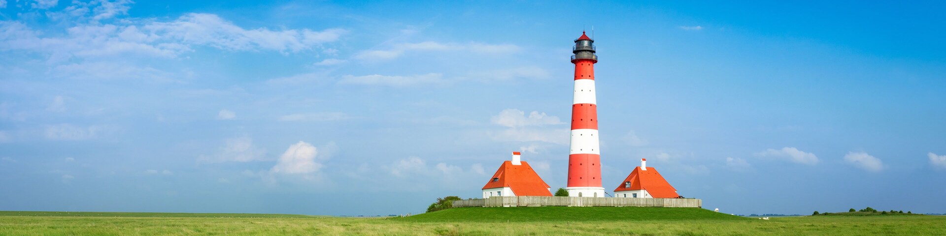 A red and white lighthouse with a wooden fence and a grassy field.