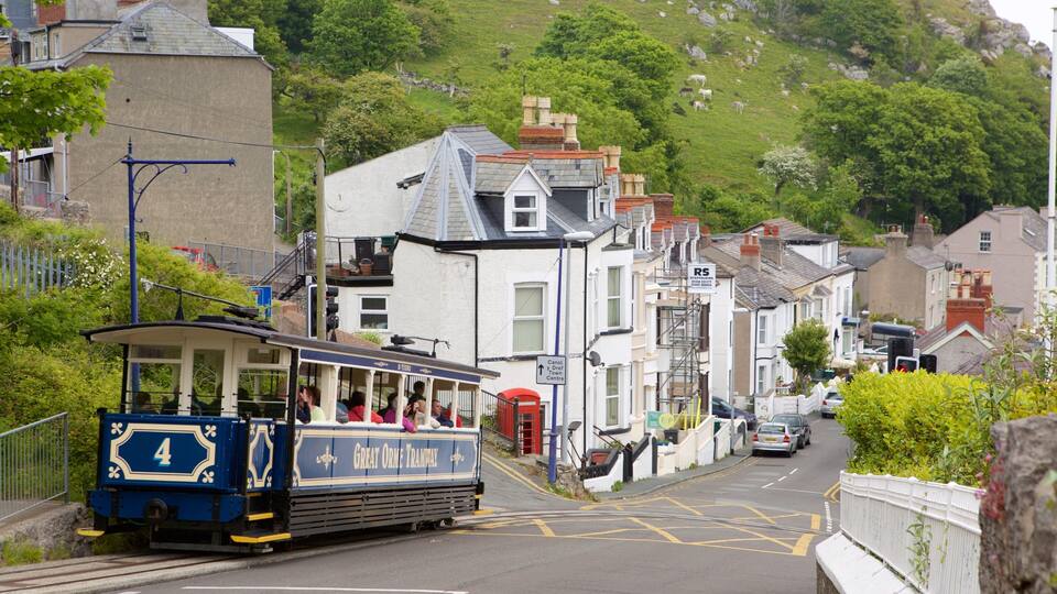 A tram on a street with buildings and a hill in the background.