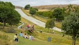 A park with a metal slide, grassy areas, trees, and a rocky hillside in the background.