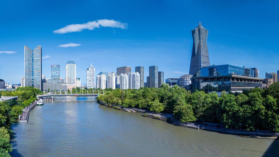 A river with a bridge, surrounded by trees and modern buildings.