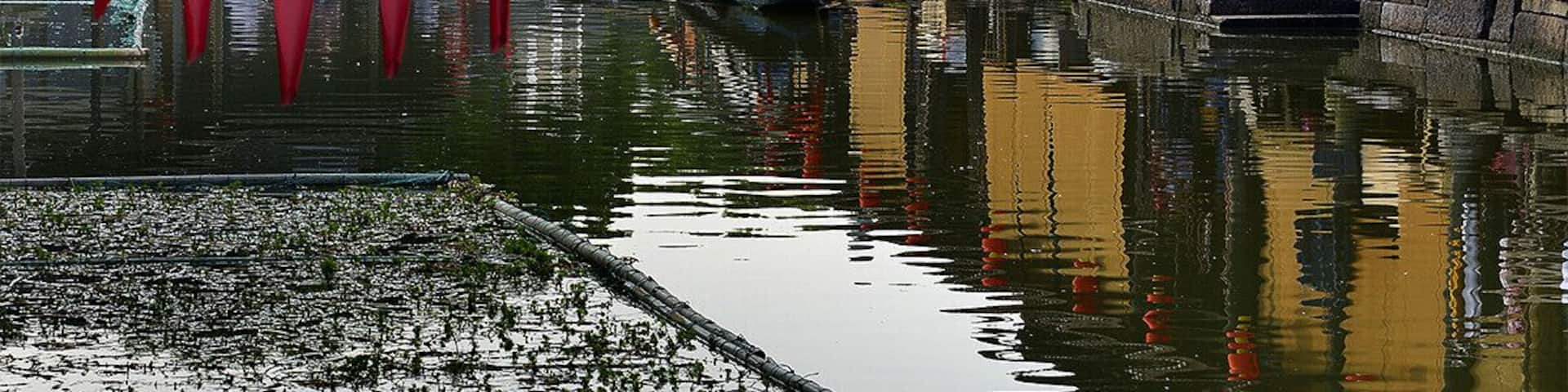 A traditional Chinese waterway with a boat, wooden buildings, and red lanterns.