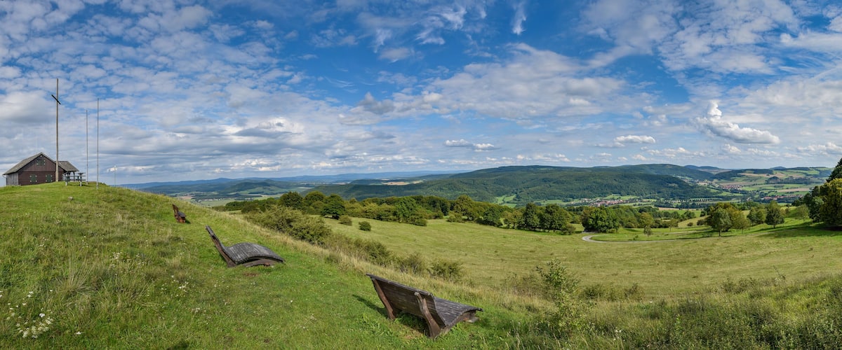 A grassy hill with a wooden bench, a small wooden structure, and a winding road in the distance.
