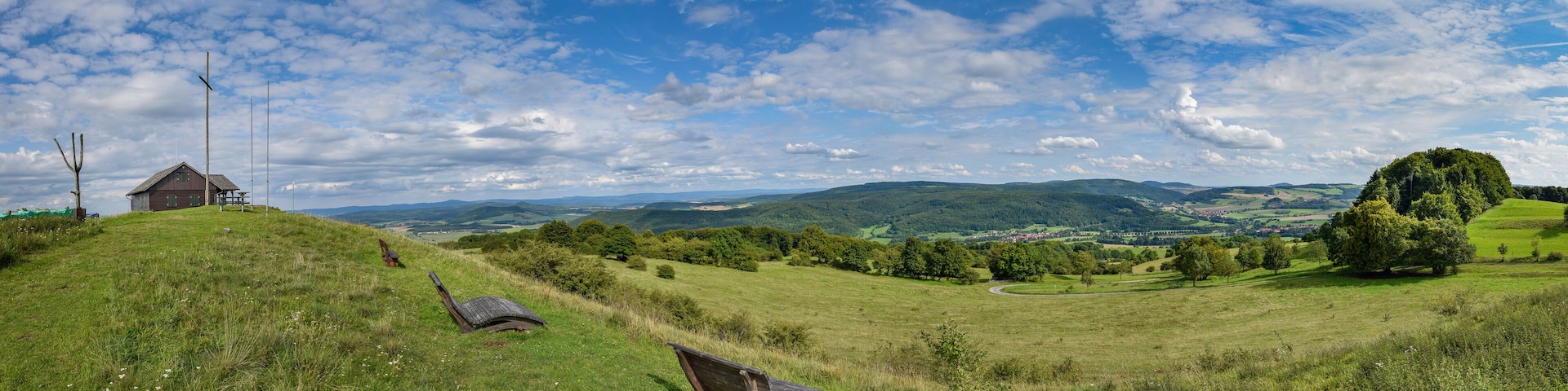 A grassy hill with a wooden bench, a small wooden structure, and a winding road in the distance.
