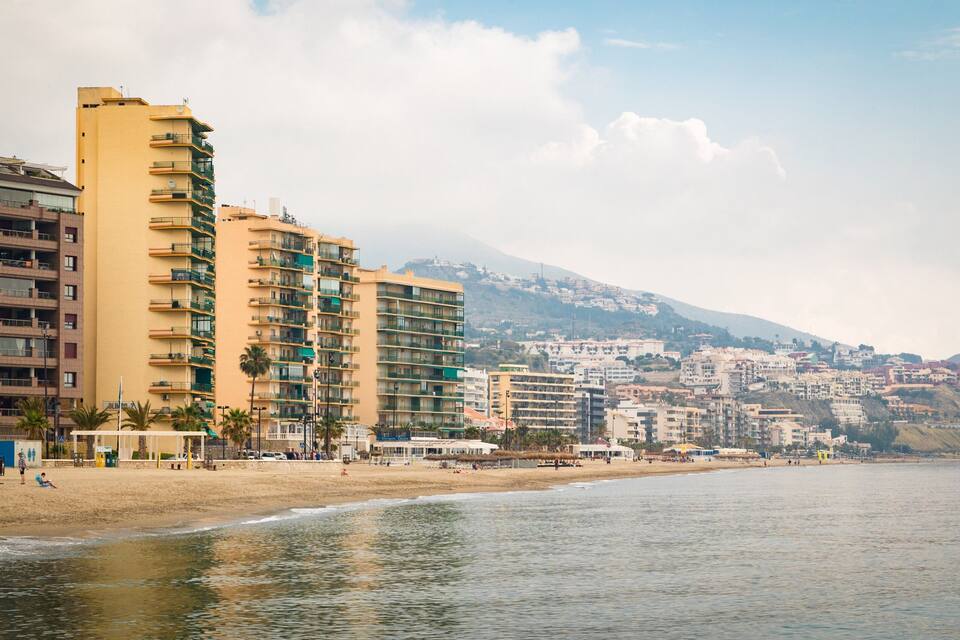 A coastal cityscape with high-rise buildings, a beach, and a mountain in the background.