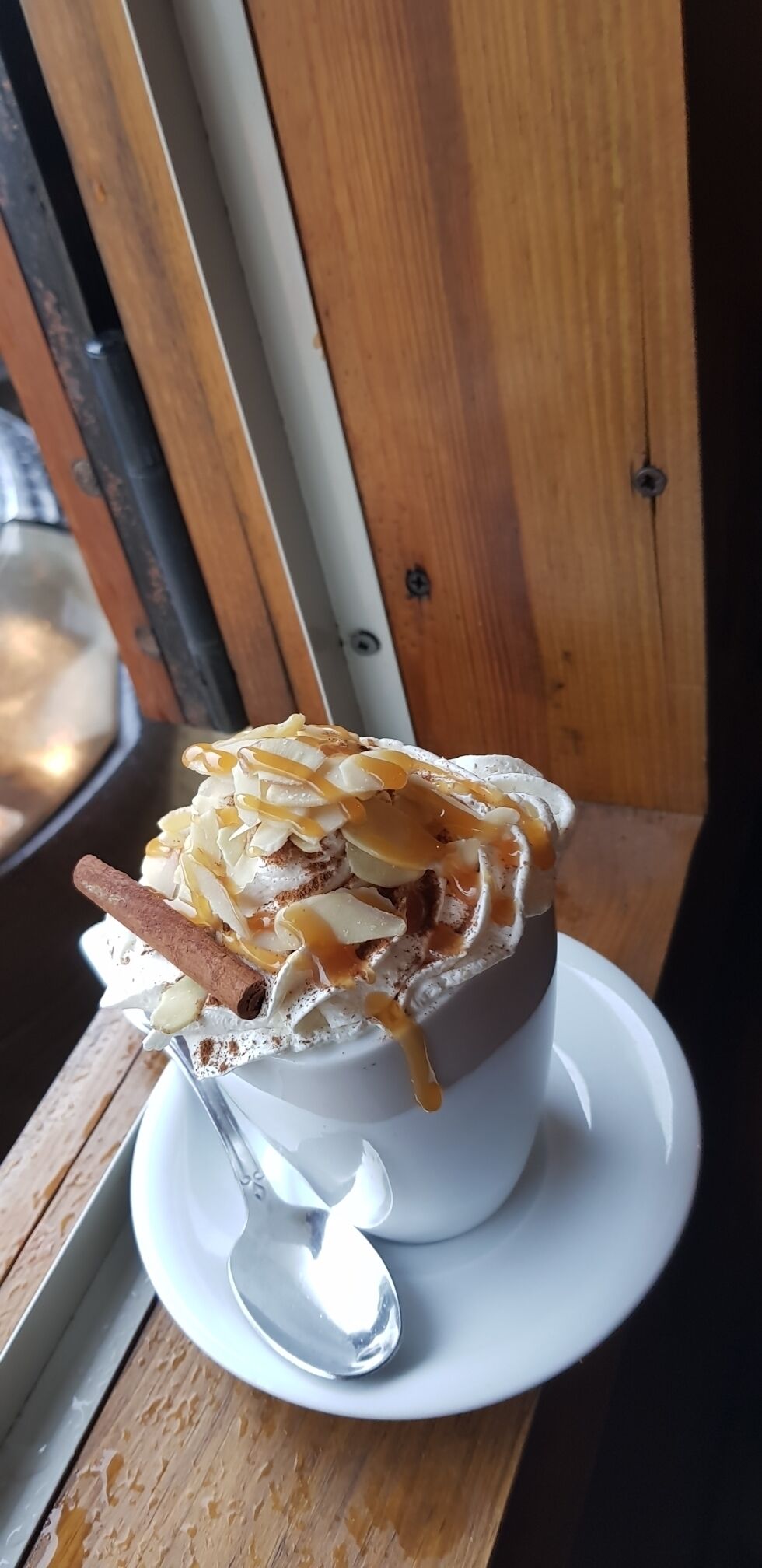 A dessert in a white cup with a spoon on a saucer.