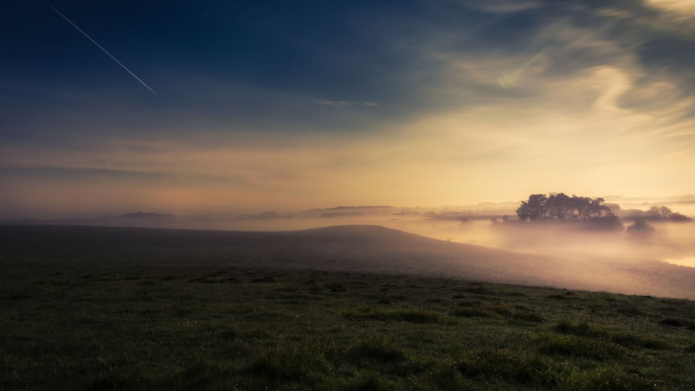 Eine neblige Landschaft mit klarem Himmel, einer fernen Baumgrenze und einer sichtbaren Flugzeugspur.