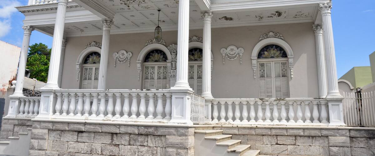A white colonial-style building with a balcony, columns, and decorative arches.