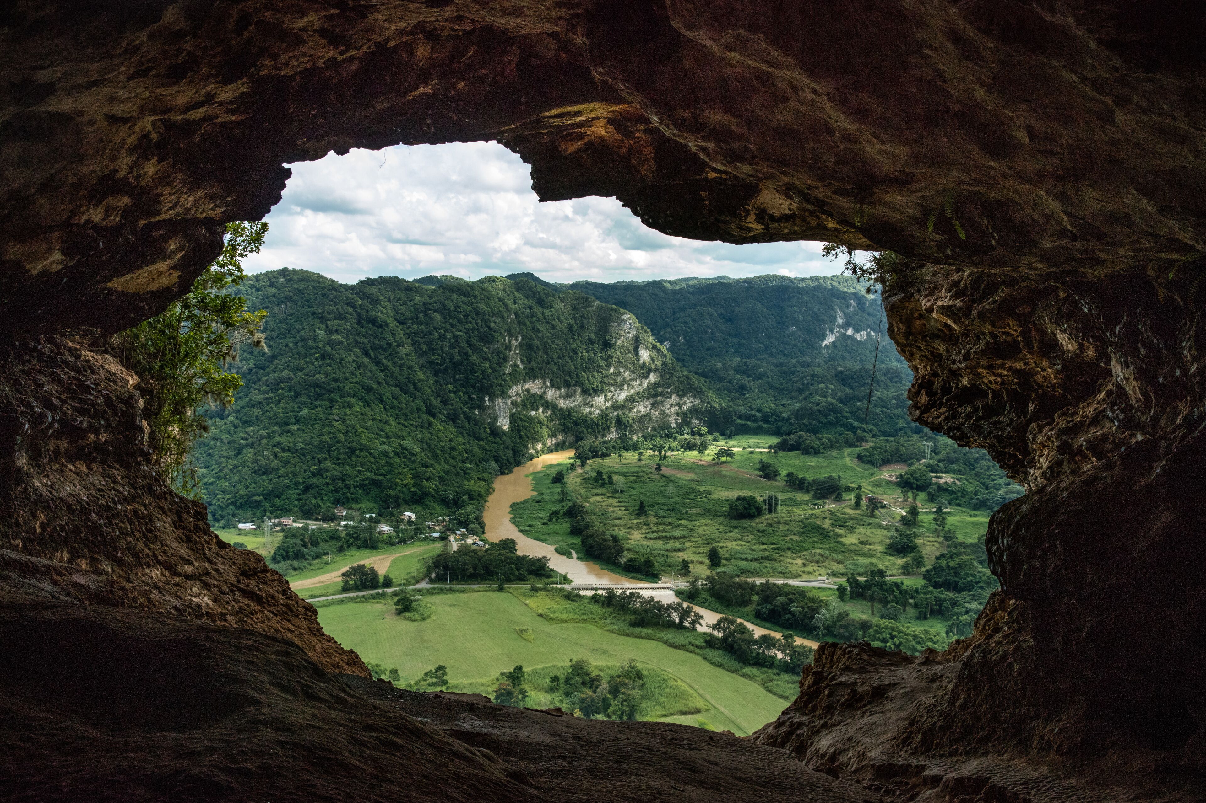 A valley through a cave opening, with a river winding through the landscape and a bridge crossing the river.