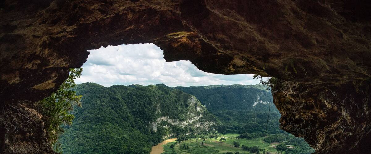 A valley through a cave opening, with a river winding through the landscape and a bridge crossing the river.