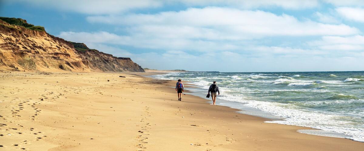 A sandy beach with footprints, a cliff, and the ocean.