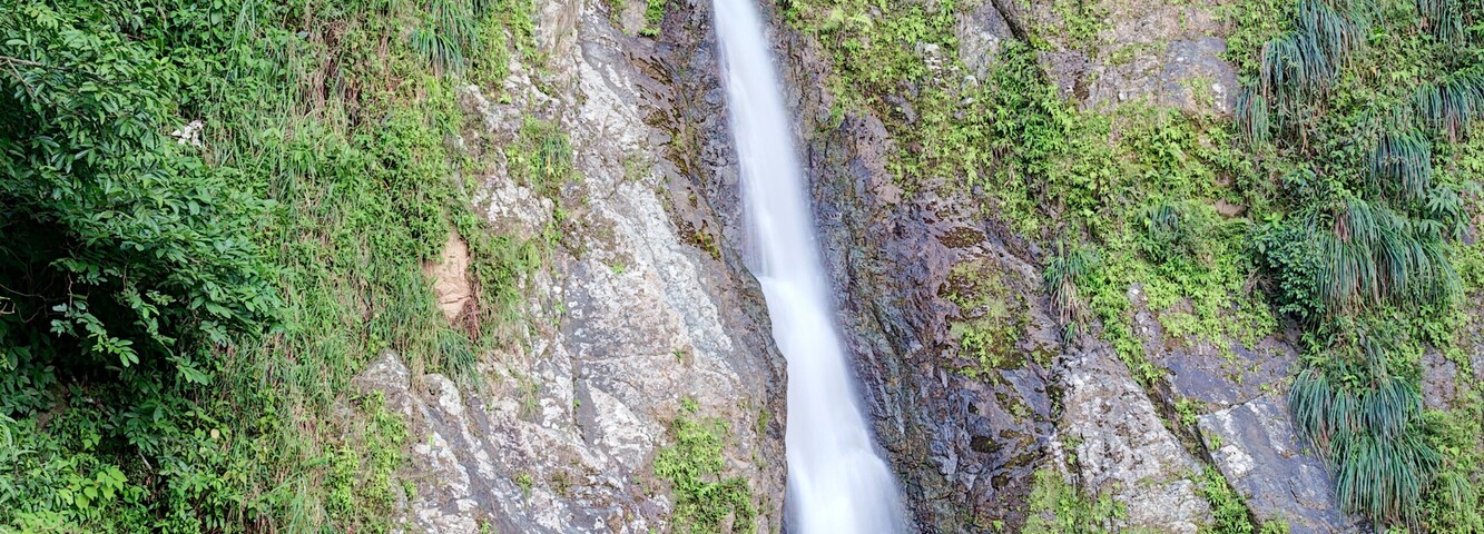 Uma cascata desce por um penhasco rochoso, rodeada por vegetação exuberante.