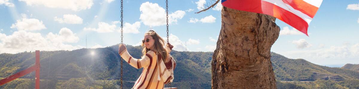 Happy girl swinging from tree over mountain landscape at Curva Del Arbol in Cayey Puerto Rico