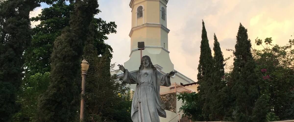 A statue of a robed figure with outstretched arms, a church tower, and a staircase leading to the tower.