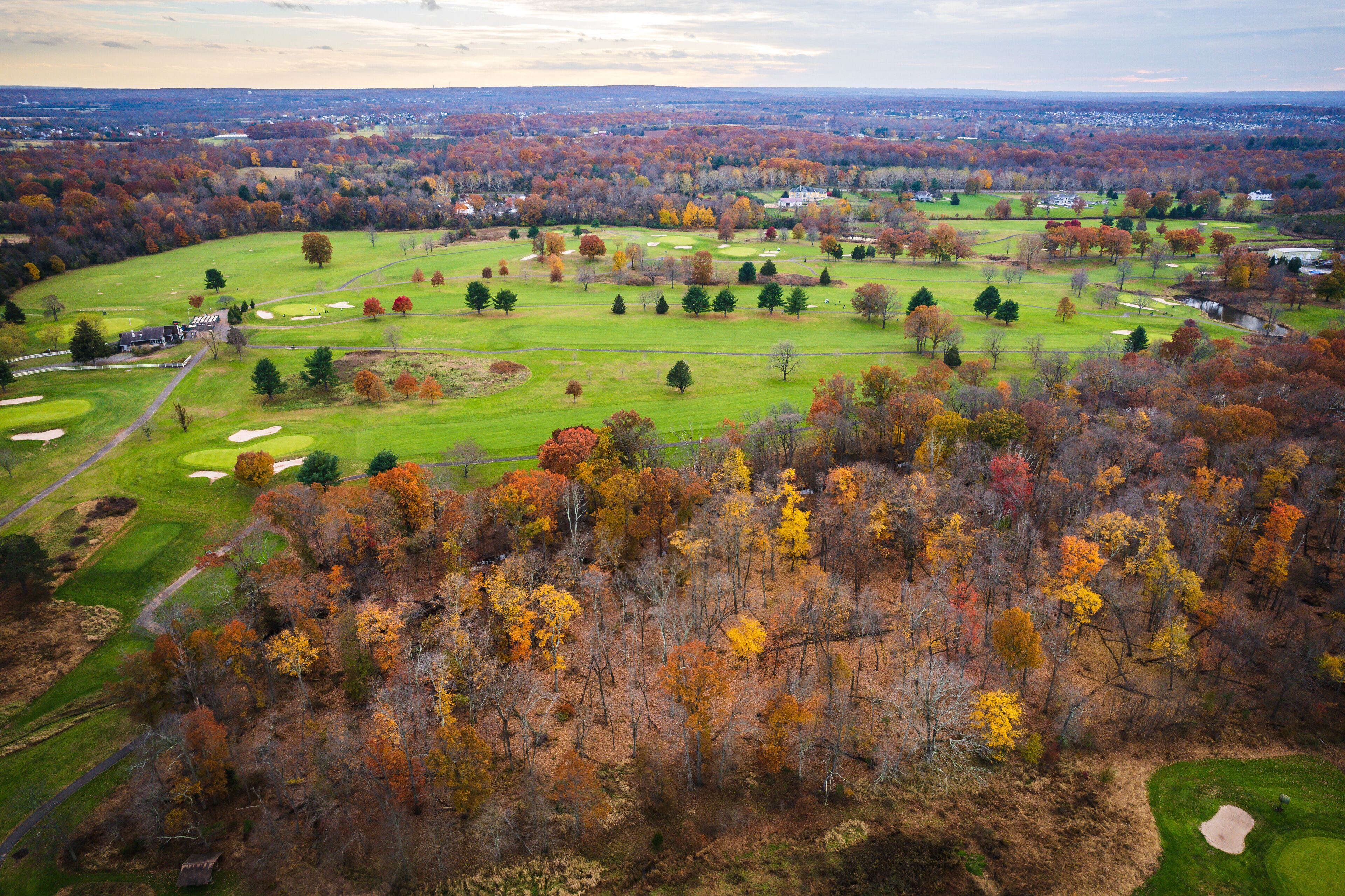A golf course surrounded by autumn-colored trees and a distant cityscape.