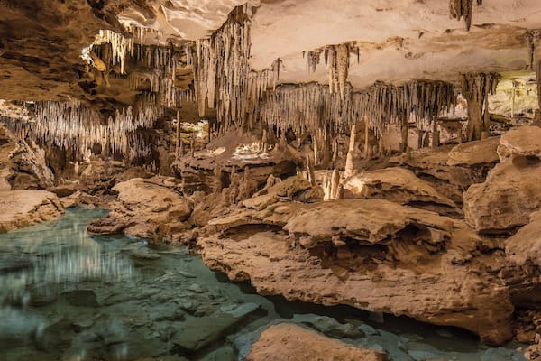 A cave with stalactites and stalagmites, a water pool, and rocky formations.