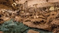 A cave with stalactites and stalagmites, a water pool, and rocky formations.