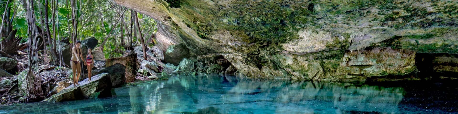 A clear blue pool with reflections of trees and rocks.