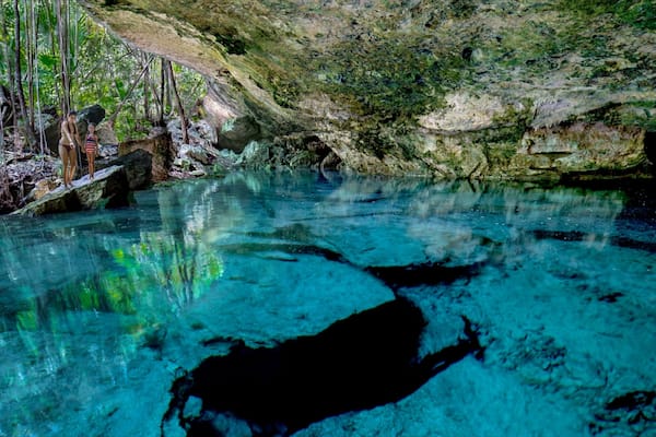 A clear blue pool with reflections of trees and rocks.