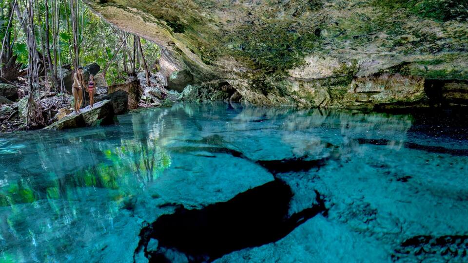 A clear blue pool with reflections of trees and rocks.