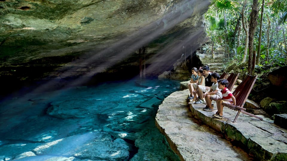 A clear blue pool with people sitting on wooden benches under a cave.