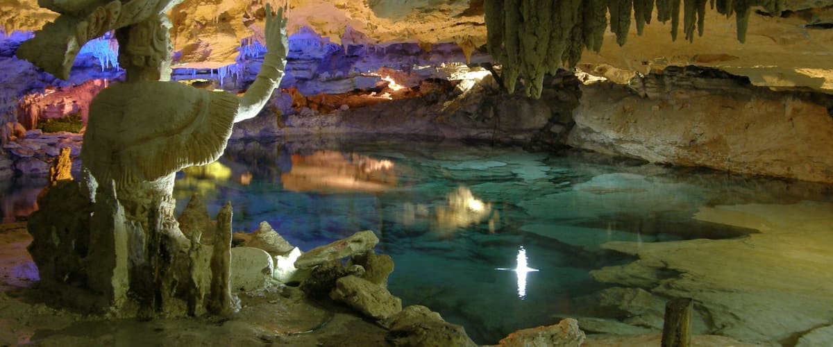 A cave with stalactites, stalagmites, and a reflective pool.