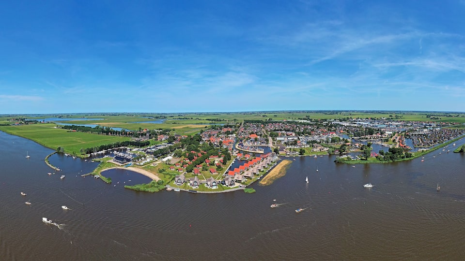 An aerial view of a riverside town with boats, a bridge, and surrounding green fields.