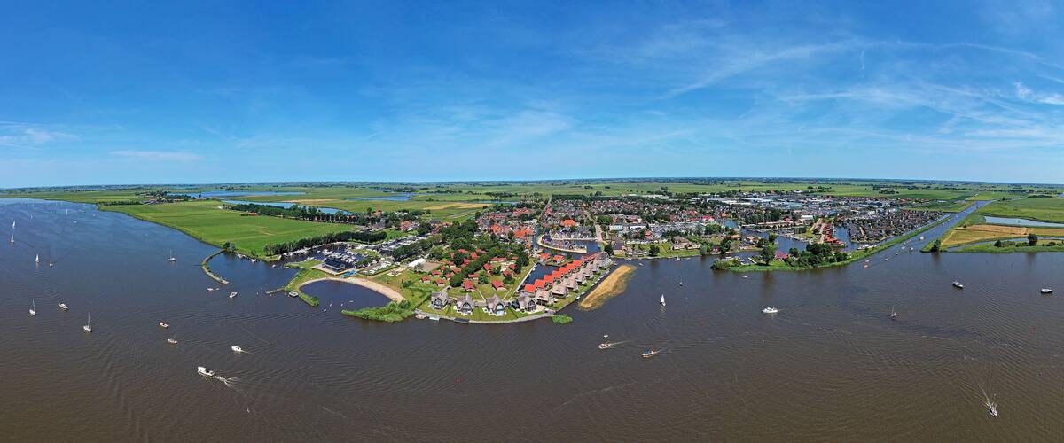 An aerial view of a riverside town with boats, a bridge, and surrounding green fields.