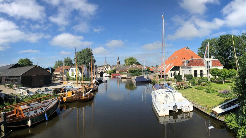 A canal with boats, a church, and houses with red roofs.