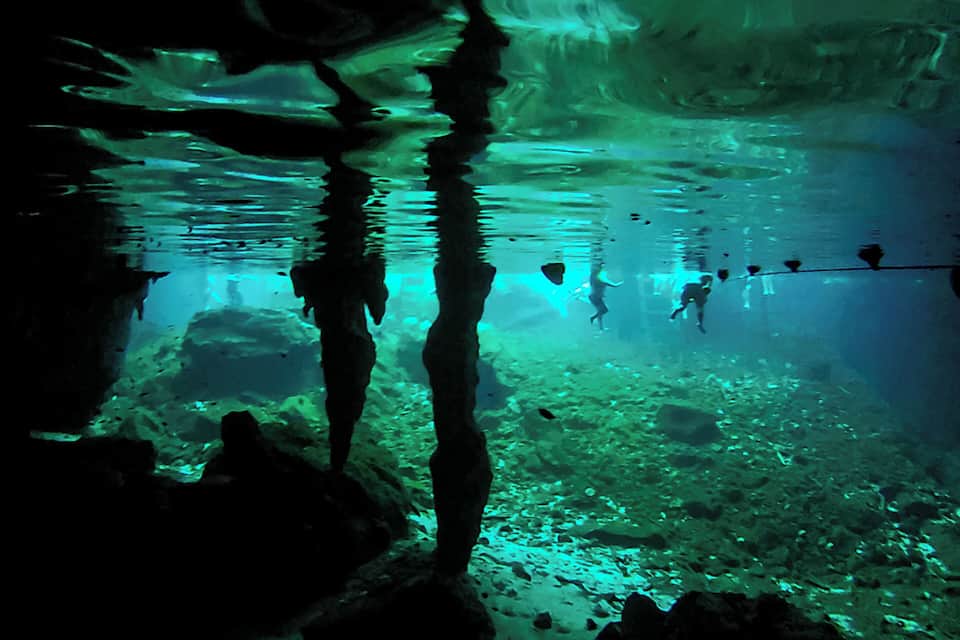 Una cueva submarina con estalactitas y estalagmitas, iluminada por luces verdes.